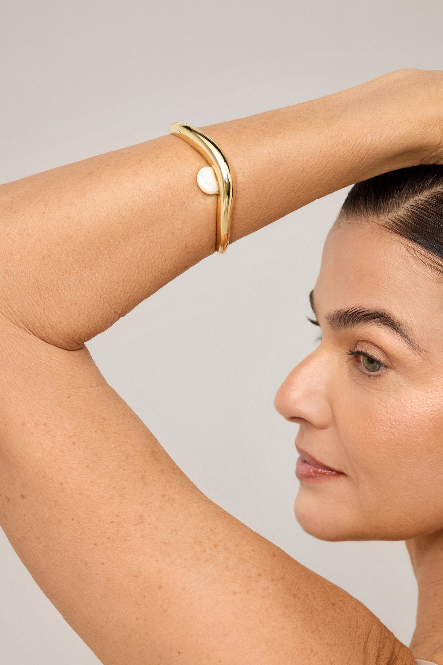 Bracelete dourado com madrepérola central e linhas fluidas contemporâneas