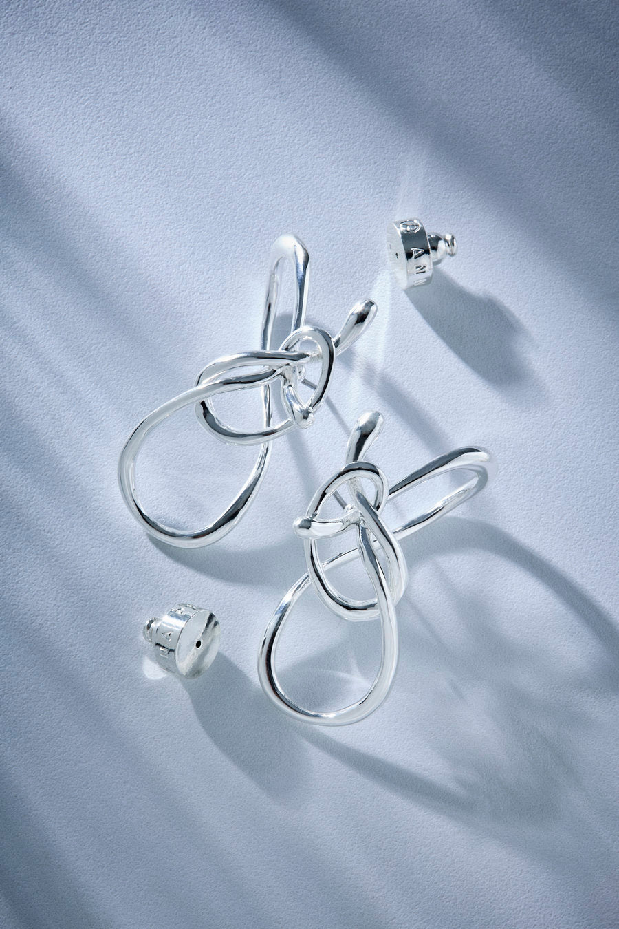 Um brinco de ouro com design orgânico e escultural, apresentando linhas sinuosas e entrelaçadas em uma composição vazada. A peça transmite conexão, movimento e a força das raízes por meio de uma estética contemporânea.