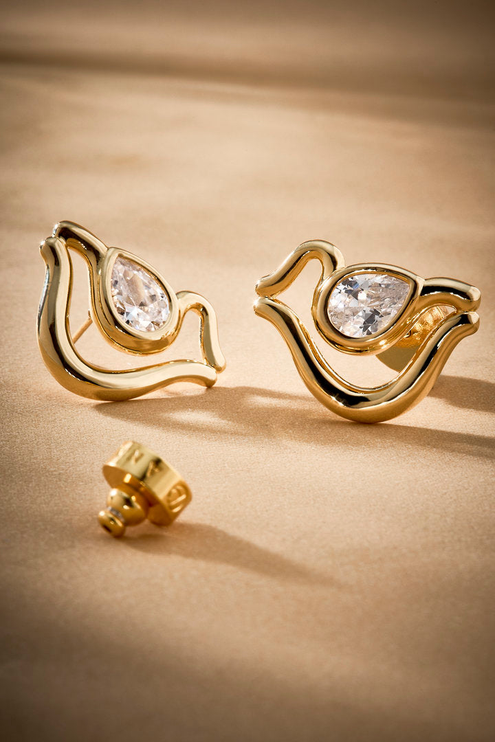 Brinco Audrey P em dourado, com curvas orgânicas e cristal austríaco em destaque. Uma joia delicada e contemporânea para composições elegantes.