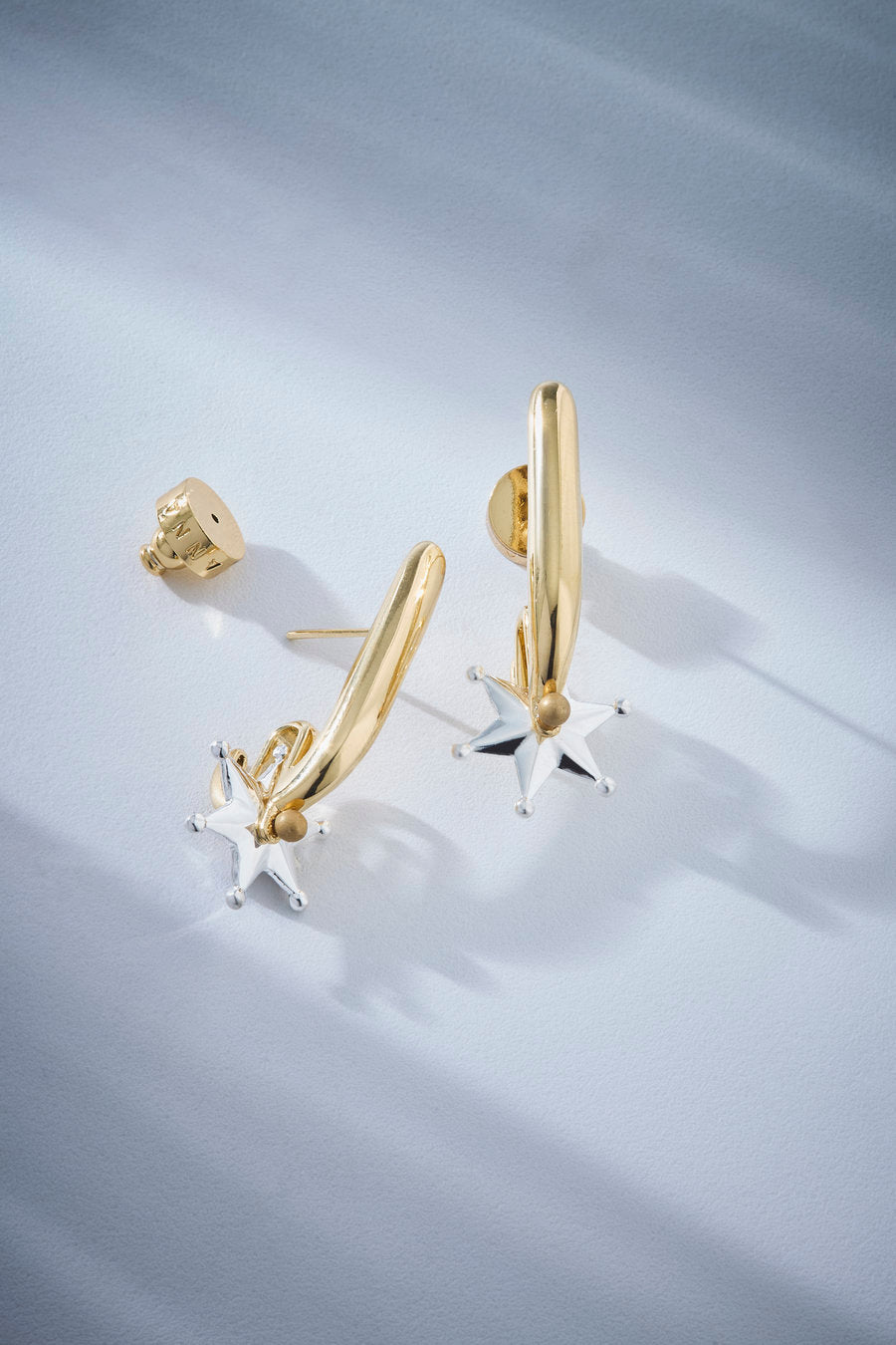 Brinco statement bicolor dourado e prata com design escultural, acabamento polido e estrela prateada, ideal para produções marcantes.