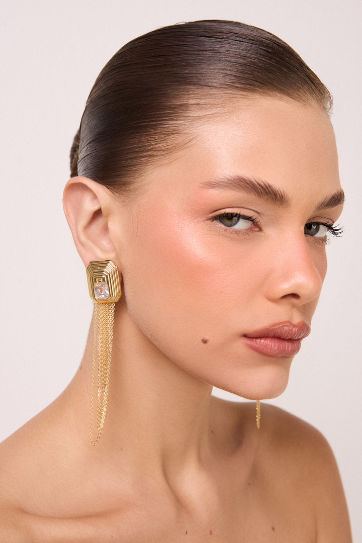 Brinco Lumier dourado com design geométrico, zircônia central e franjas em corrente para looks elegantes, marcantes e sofisticados.
