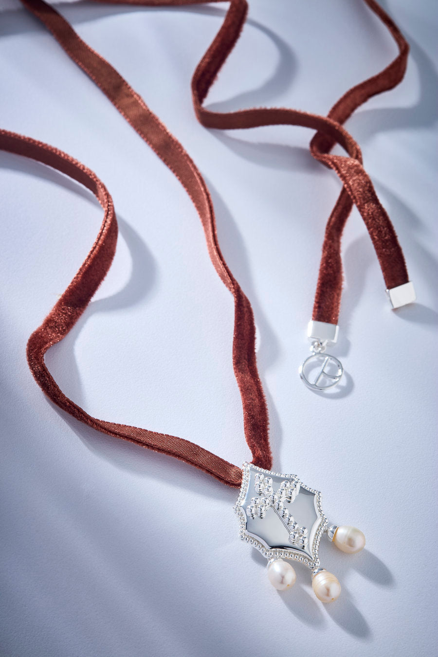 Choker Autoridade com fita de veludo preta, medalhão prata ornamental e pérolas, ideal para looks elegantes e marcantes.