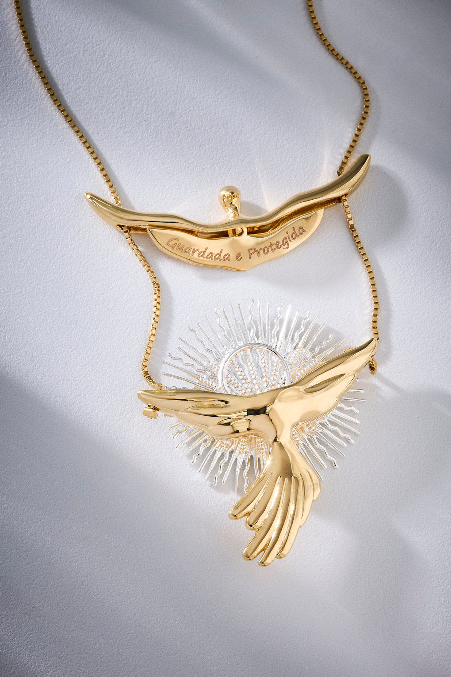 Colar dourado e prateado com pingente passaro sobre elemento radiante, em design escultural e simbólico.