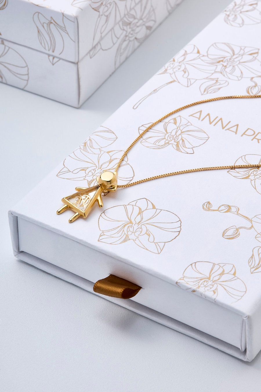 Colar É Menina dourado que simboliza a emoção da espera e o amor que nasce antes do encontro, transformando revelação em memória e início.