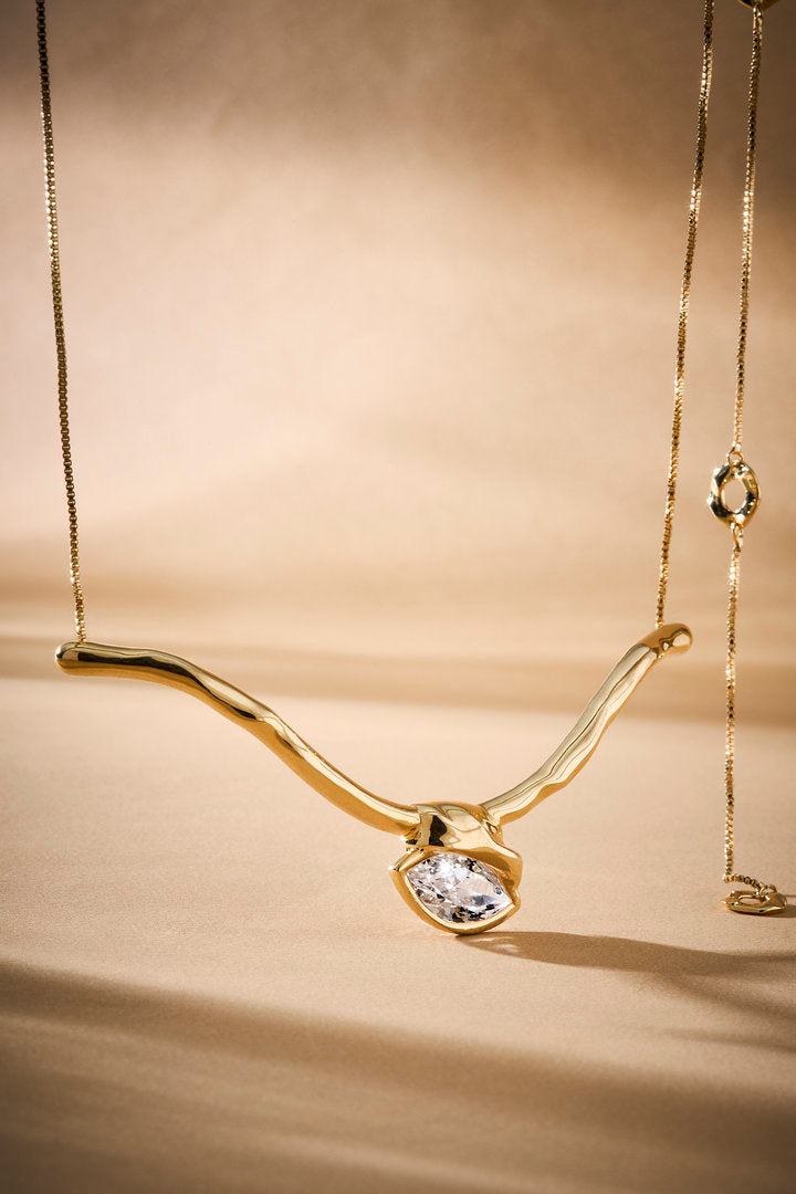 Gargantilha Gabrielle em metal de tom dourado, linhas fluidas e cristal central.