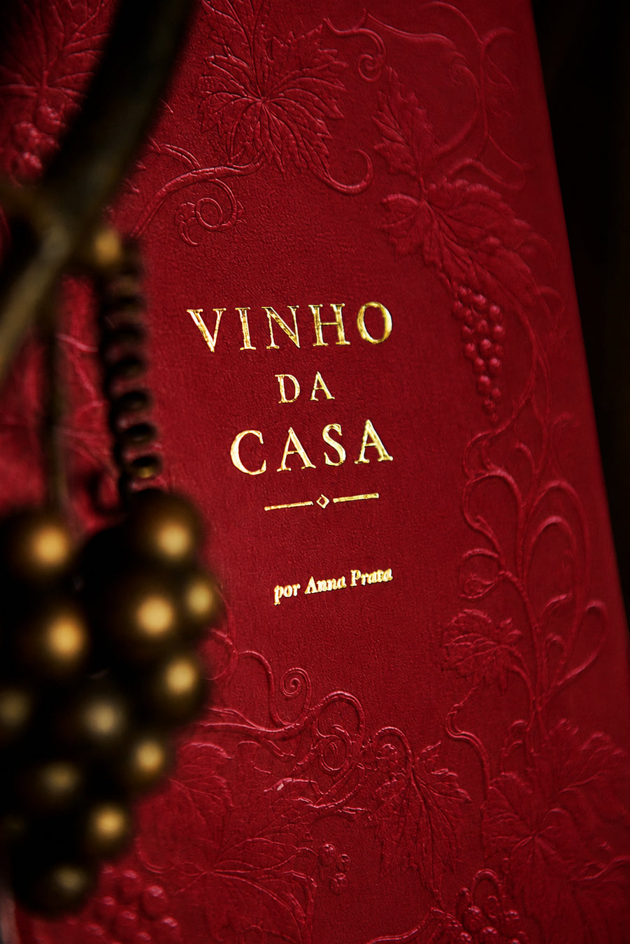 Detalhe da capa do Livro Vinho da Casa, de Anna Prata, devocional cristão e planner 2027, com acabamento bordô texturizado, videiras em relevo e tipografia dourada.