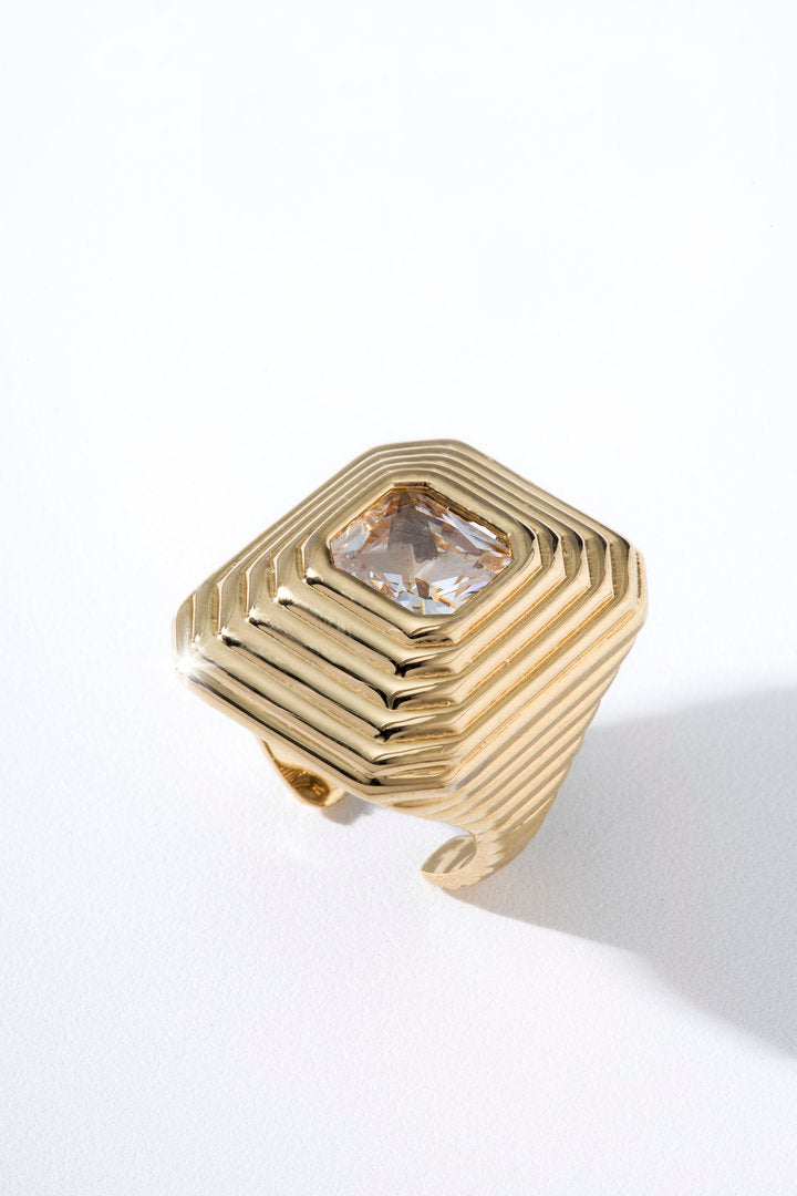 Anel Lumier dourado com design geométrico em camadas piramidais e zircônia cristal central.