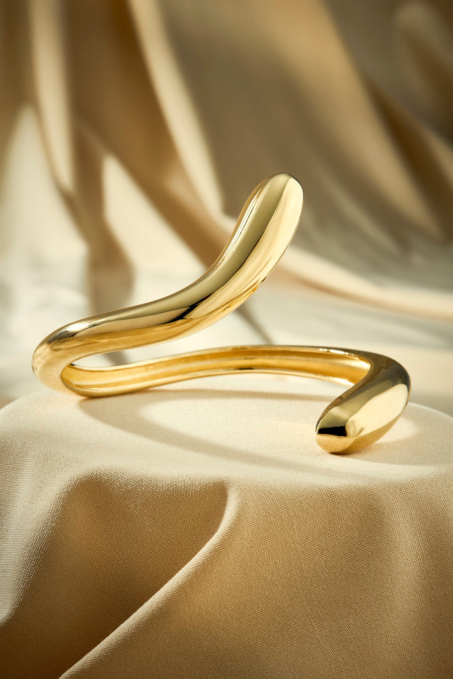 Bracelete dourado com linhas curvas e visual minimalista contemporâneo