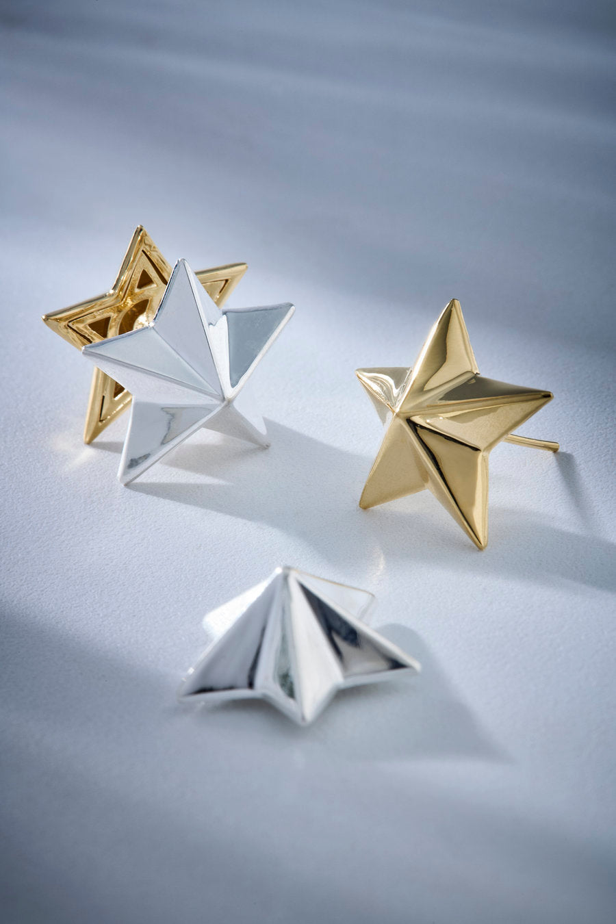Brinco em formato de estrela facetada com acabamento polido em dourado e prateado, inspirado em símbolos celestes.