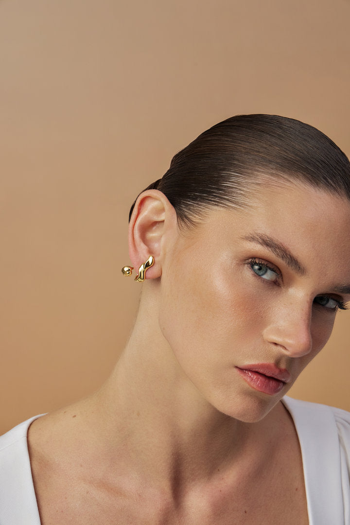 Brinco Frida em tom dourado – curvas orgânicas e esfera metálica – design escultural e contemporâneo