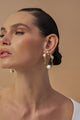 Uma modelo elegante usa brincos Gabrielle em tom dourado, com formas orgânicas, pérolas e cristais austríacos.
