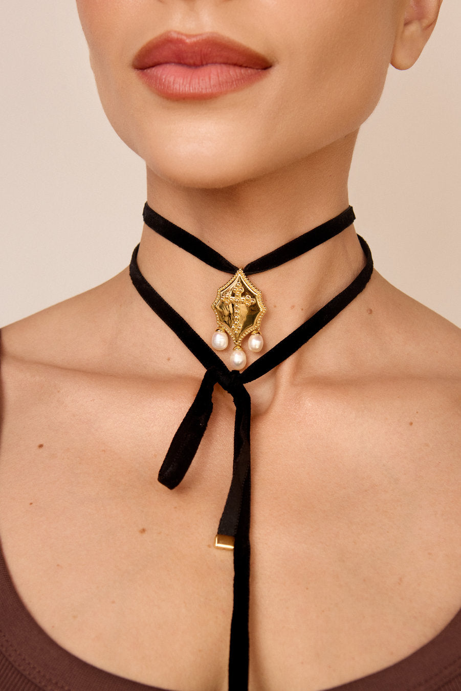 Modelo usando choker de veludo preto com pingente dourado em relevo e pérolas, joia sofisticada para looks elegantes.