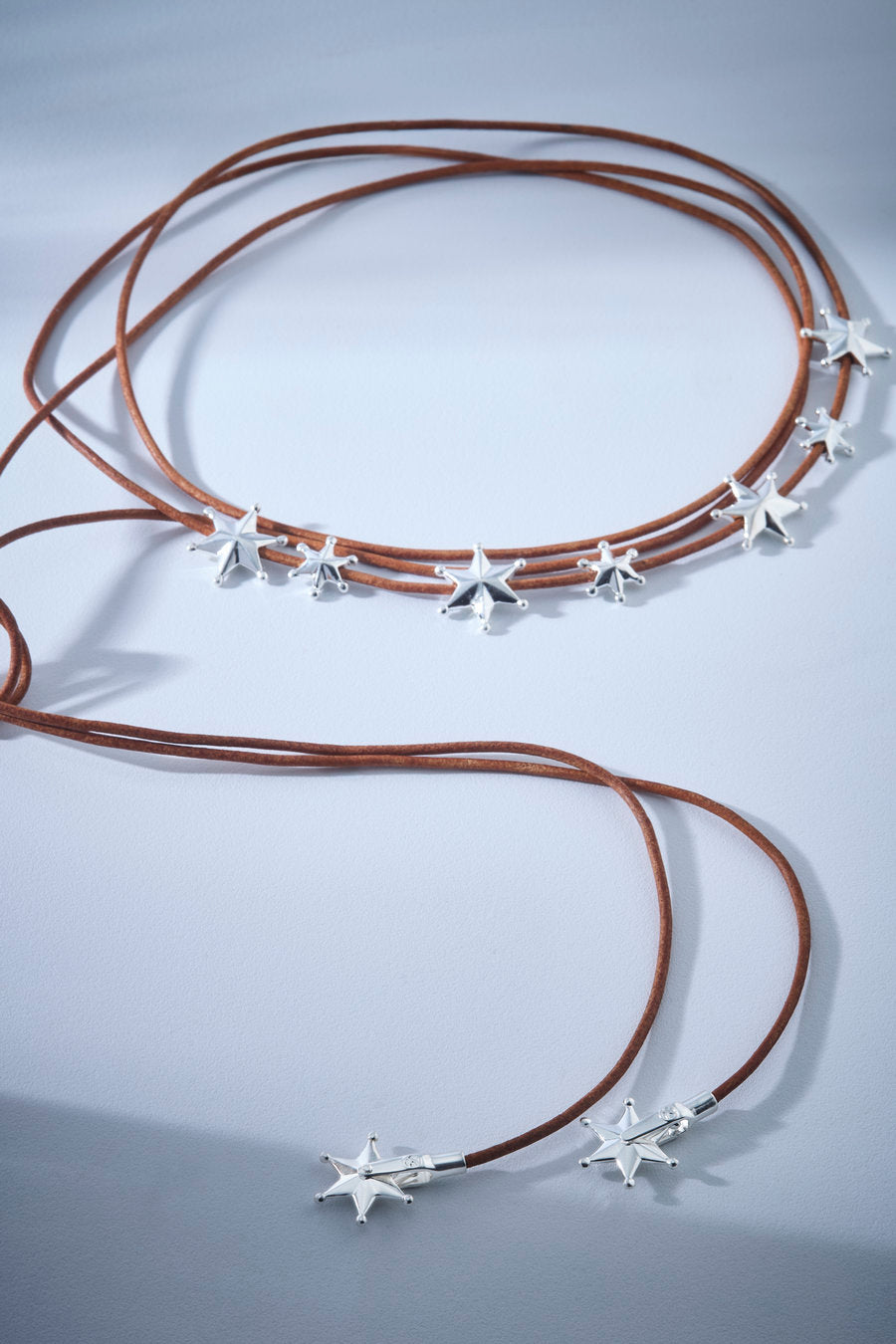 Colar Autoridade com cordão marrom e estrelas prateadas, um acessório moderno e marcante para looks cheios de personalidade.