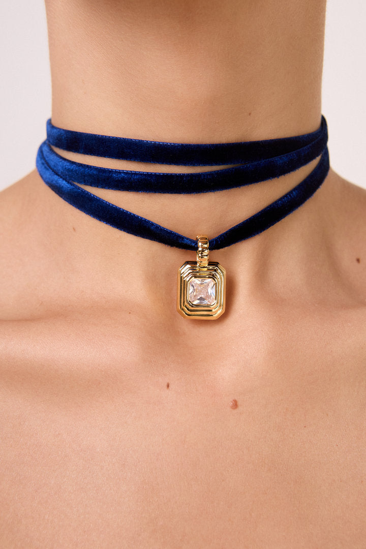 Colar Lumier com fita de veludo azul e pingente dourado com zircônia, ideal para looks modernos, elegantes e versáteis.
