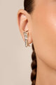 Earhook prata com design escultural e polido, formato alongado e base estruturada em curvas, de visual moderno e autoral.