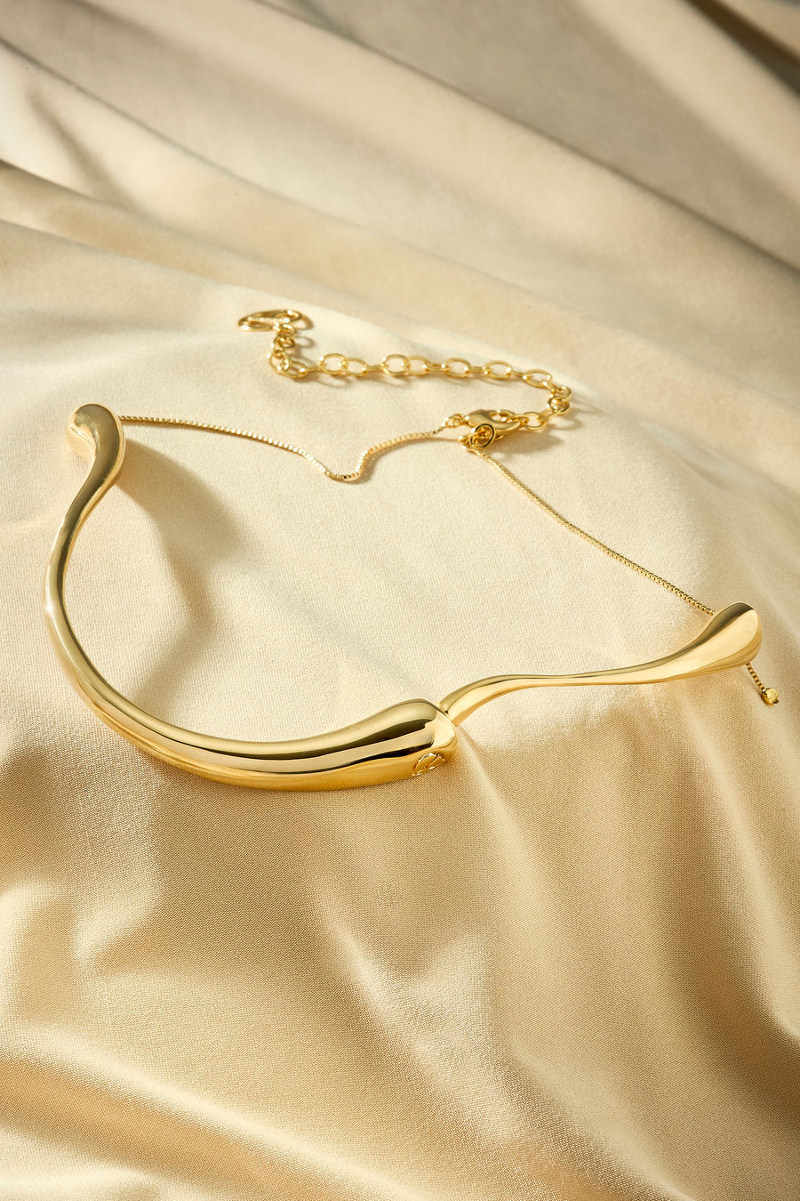 Gargantilha dourada com linhas curvas e visual minimalista contemporâneo