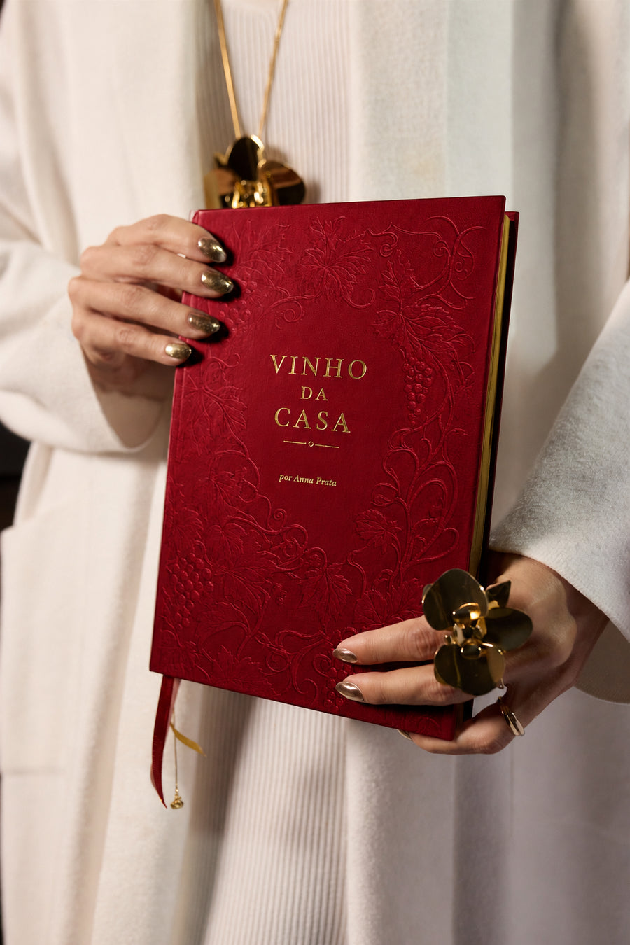 Anna Prata segurando o Livro Vinho da Casa 2027, devocional cristão e planner anual feminino, com capa dura bordô, videiras em relevo e detalhes dourados.