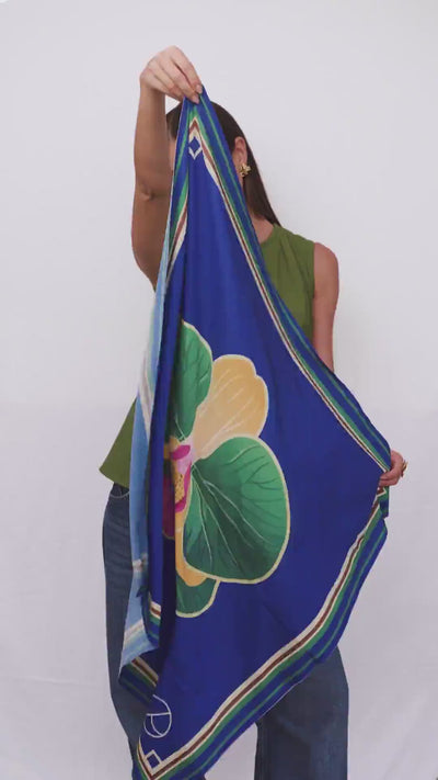Lenço Tropicália com estampa de orquídeas, folhagens verdes e azul vibrante em composição tropical.