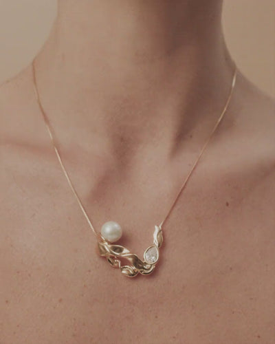 Colar Audrey dourado e prata com pérola, cristal austríaco e formas fluidas que evocam o encanto do cinema clássico.