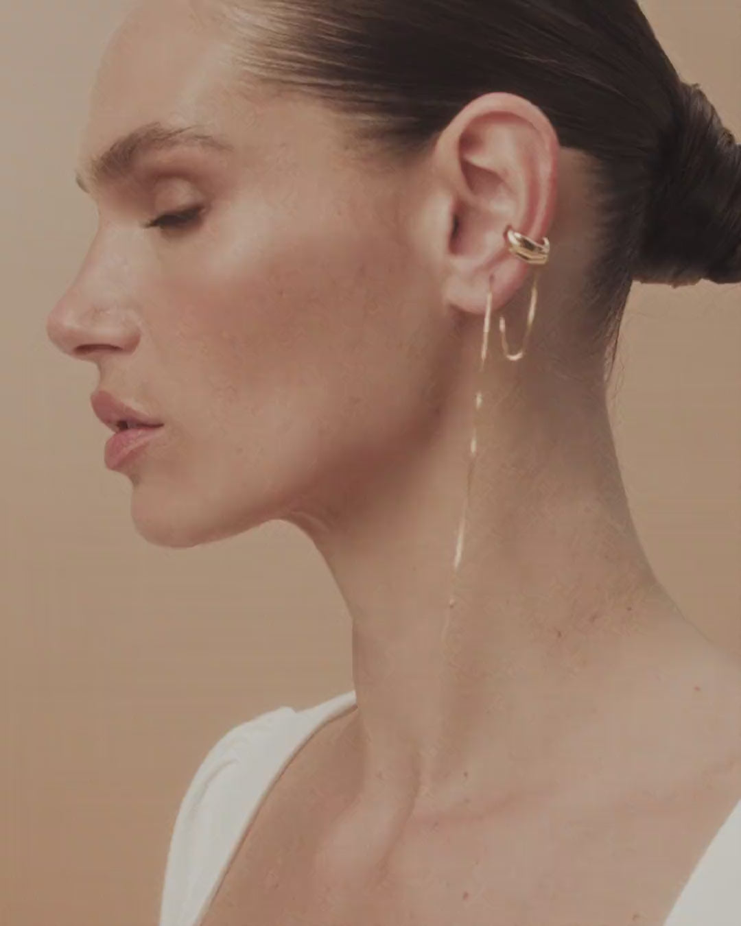 Piercing Frida dourado e  prateado, com curvas esculturais e correntes fluidas que lembram tinta percorrendo a tela.